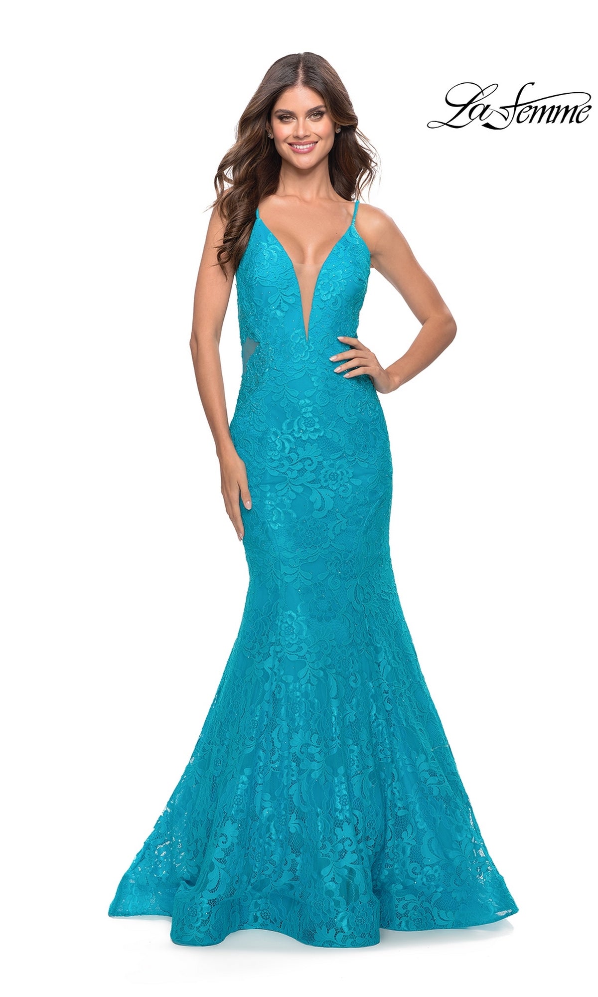 Woman modeling La Femme 31512, a sleeveless turquoise long lace mermaid prom dress with a deep V neckline, stands smiling with one hand on her hip.